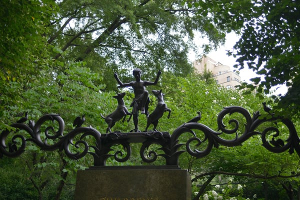 Bronze sculpture on ornate iron gate surrounded by summer foliage
